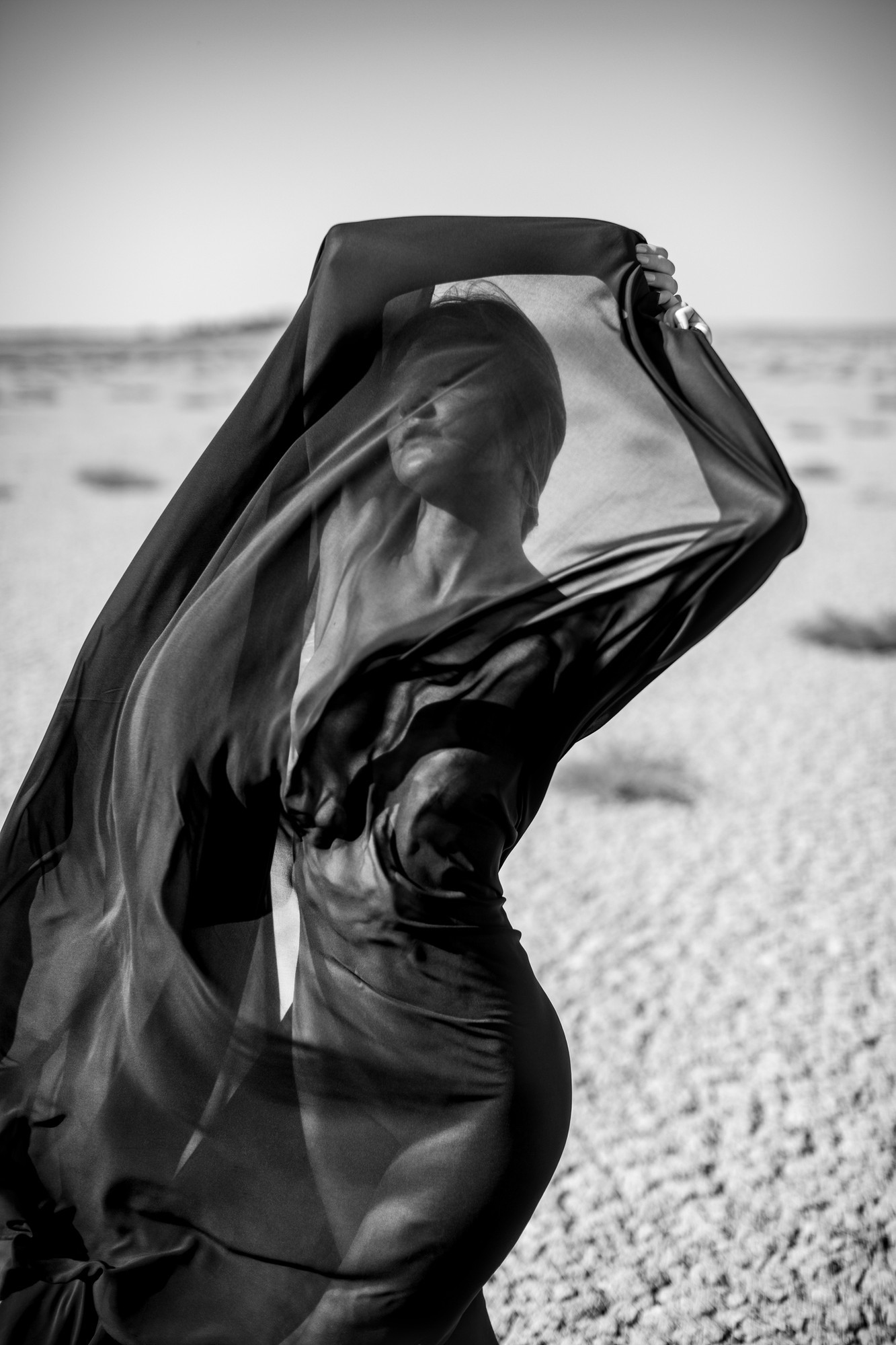Artistic abstract portrait of woman covered with black fabric in desert